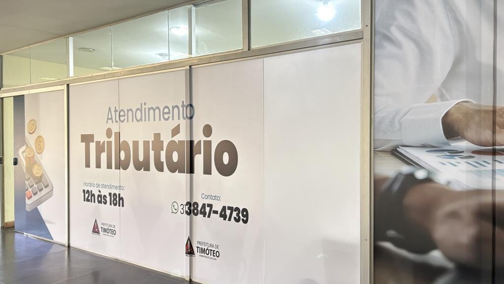 Fachada interna do Atendimento Tributário da Prefeitura de Timóteo, com horário das 12h às 18h e telefone de contato
