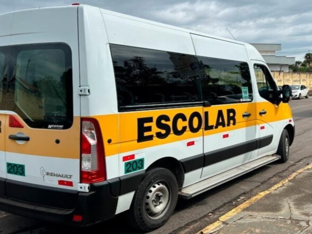 Van branca de transporte escolar estacionada em uma rua de Timóteo, com faixa amarela e a palavra Escolar na lateral